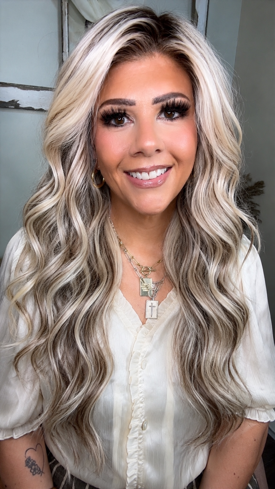 April H smiling in a white blouse with long, softly waved blonde hair and a cross necklace